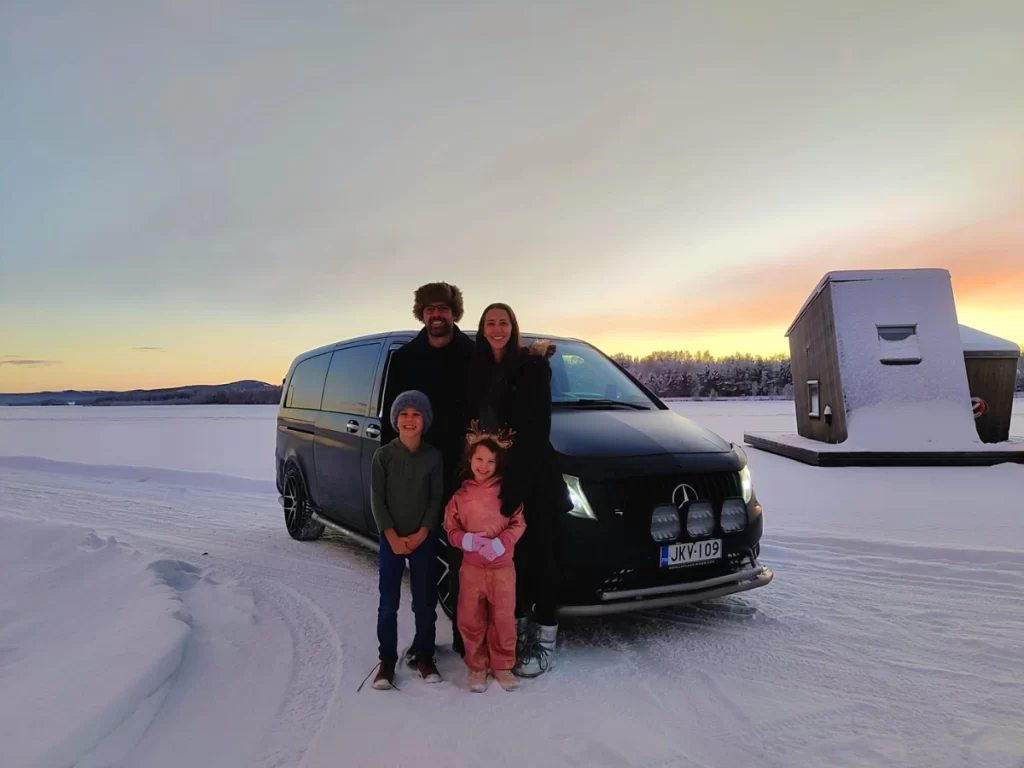 Family with children standing beside a private minivan in snowy Lapland